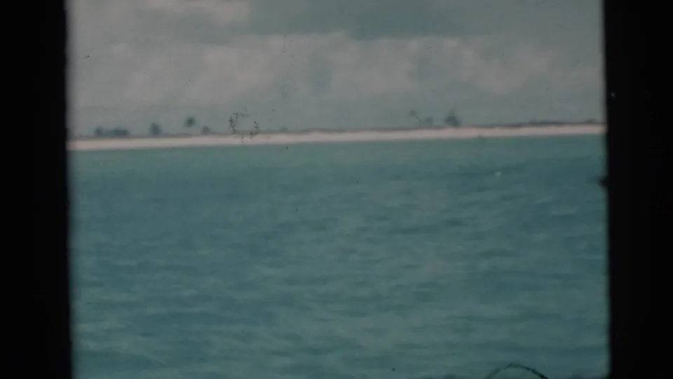1956 Miami-area home-movie frame showing blue water, a faint low island, and cloud cover on the horizon.