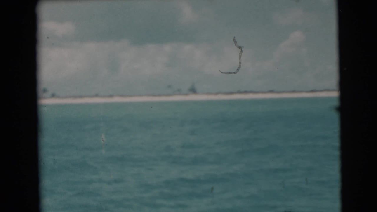 Turquoise water stretches toward a distant pale shoreline under cloudy sky.