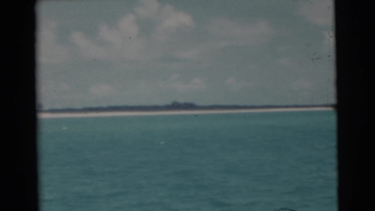 Turquoise open water with a low distant shoreline beneath a cloudy sky.