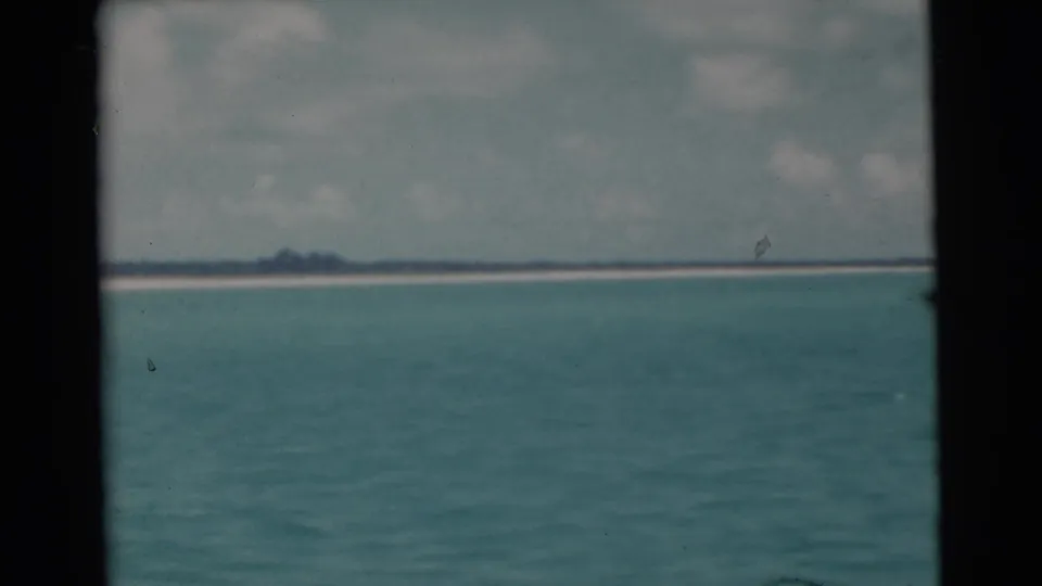 1956 Miami-area 8mm view of calm blue-green water with a pale distant shore and cloudy sky beyond the film gate.