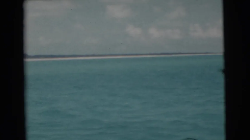1956 Miami-area home-movie frame with open water filling the foreground and a thin distant landline below clouds.