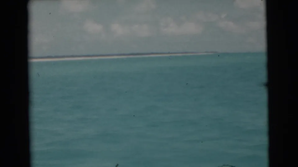 1956 Miami-area 8mm frame showing rippled blue-green water, low distant shoreline, cloudy sky, and dark film borders.