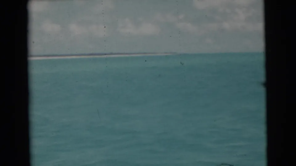 1956 Miami-area 8mm frame showing open turquoise water, a low horizon, cloudy sky, and dark film gate edges.