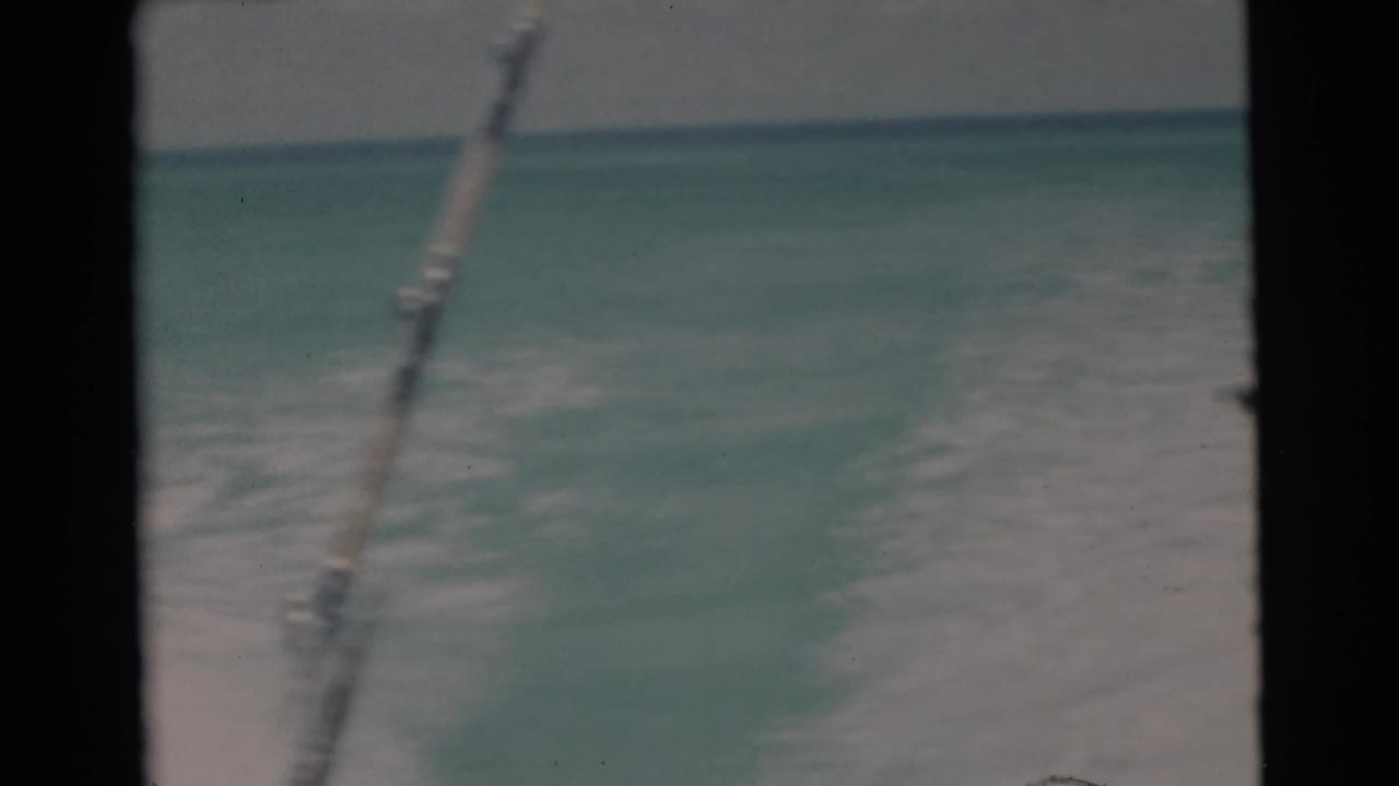 1956 Florida Keys home-movie frame with turquoise water, boat wake, and a fishing rod or line visible against the horizon.