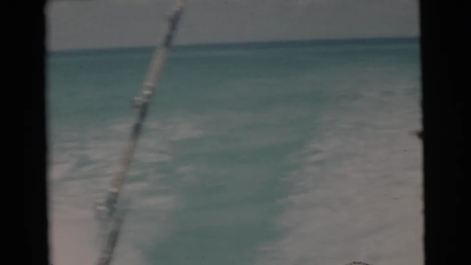 1956 Florida Keys home-movie frame with turquoise water, boat wake, and a fishing rod or line visible against the horizon.