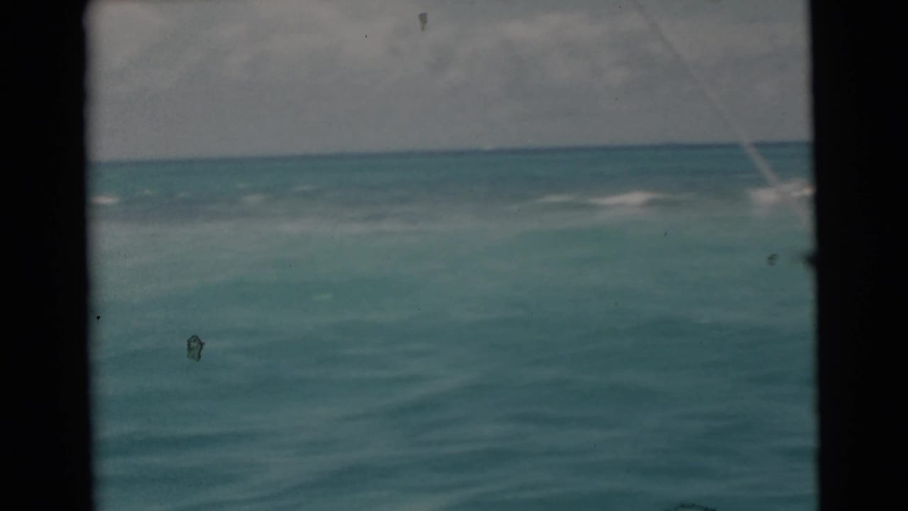 Turquoise ocean and cloudy sky seen past a dark boat edge, with a faint fishing line crossing the frame.