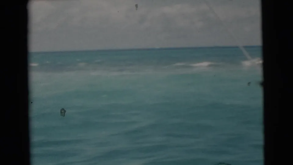 1956 Miami 8mm frame showing open turquoise water, cloudy sky, dark boat-edge framing, and a faint fishing line from a moving boat.