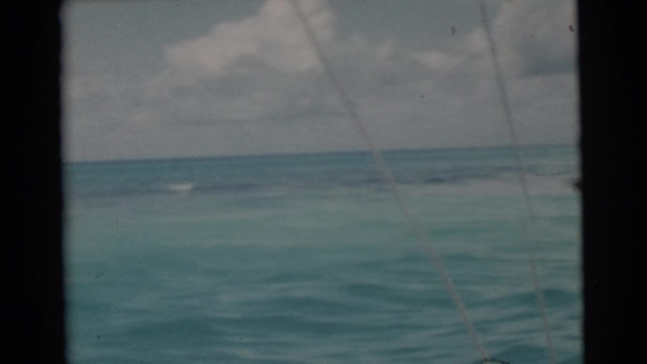 1956 Miami 8mm view of rolling turquoise water and a cloudy horizon, with dark boat framing and a faint diagonal fishing line.