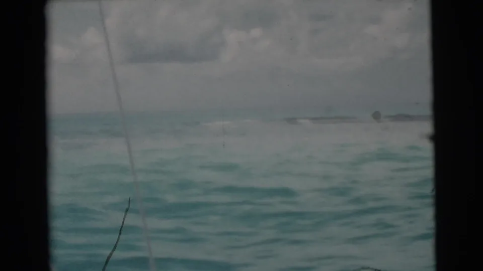 1956 Miami home-movie frame showing choppy turquoise water, cloudy sky, distant horizon, and a diagonal fishing line in the foreground.