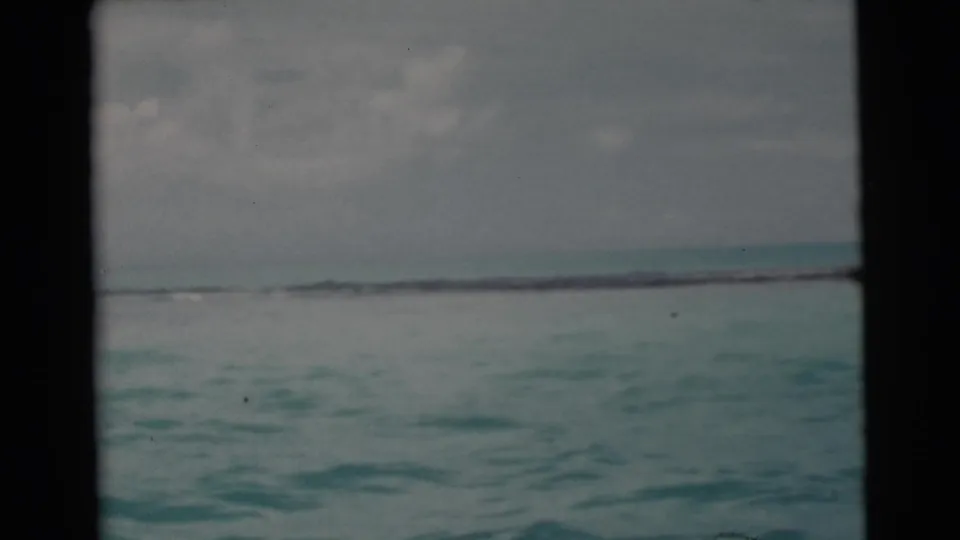 1956 Miami 8mm frame of pale turquoise ocean beneath a cloudy sky, bordered by dark film or boat edges and marked by visible film wear.
