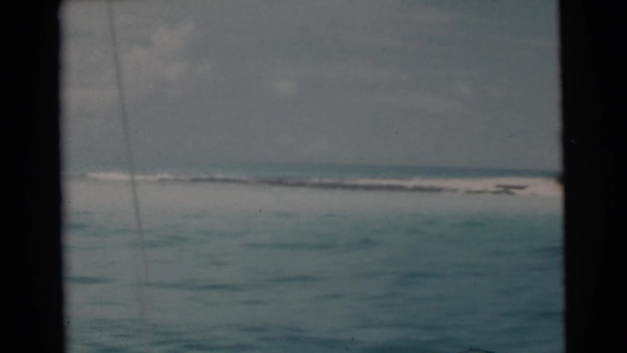 Turquoise water and distant pale beach seen through dark boat-window edges.