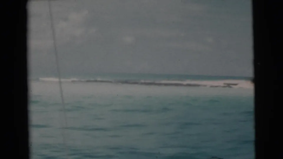 1956 Miami-area 8mm frame showing green-blue ocean, a distant pale shoreline, and dark vertical window framing from a moving boat.