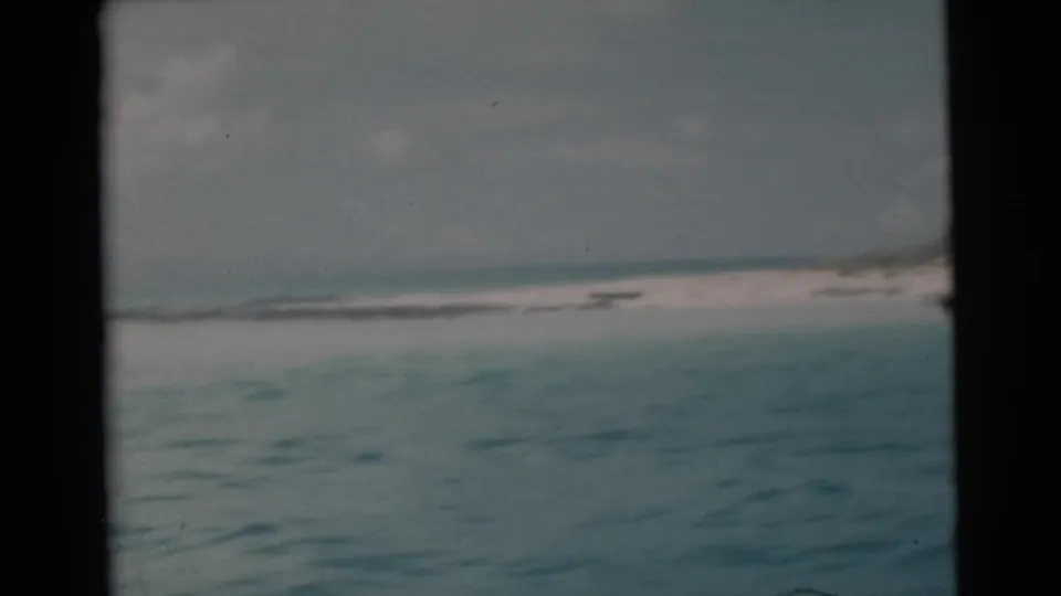 1956 Miami-area 8mm view of calm tropical water and a low beach horizon, partially bordered by the boat window or frame edge.