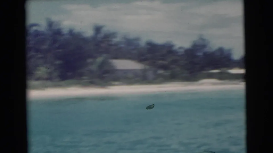 Mid-1950s Florida boat footage showing a blurred shoreline with blue water, sand, palms, and a modest building near the beach.
