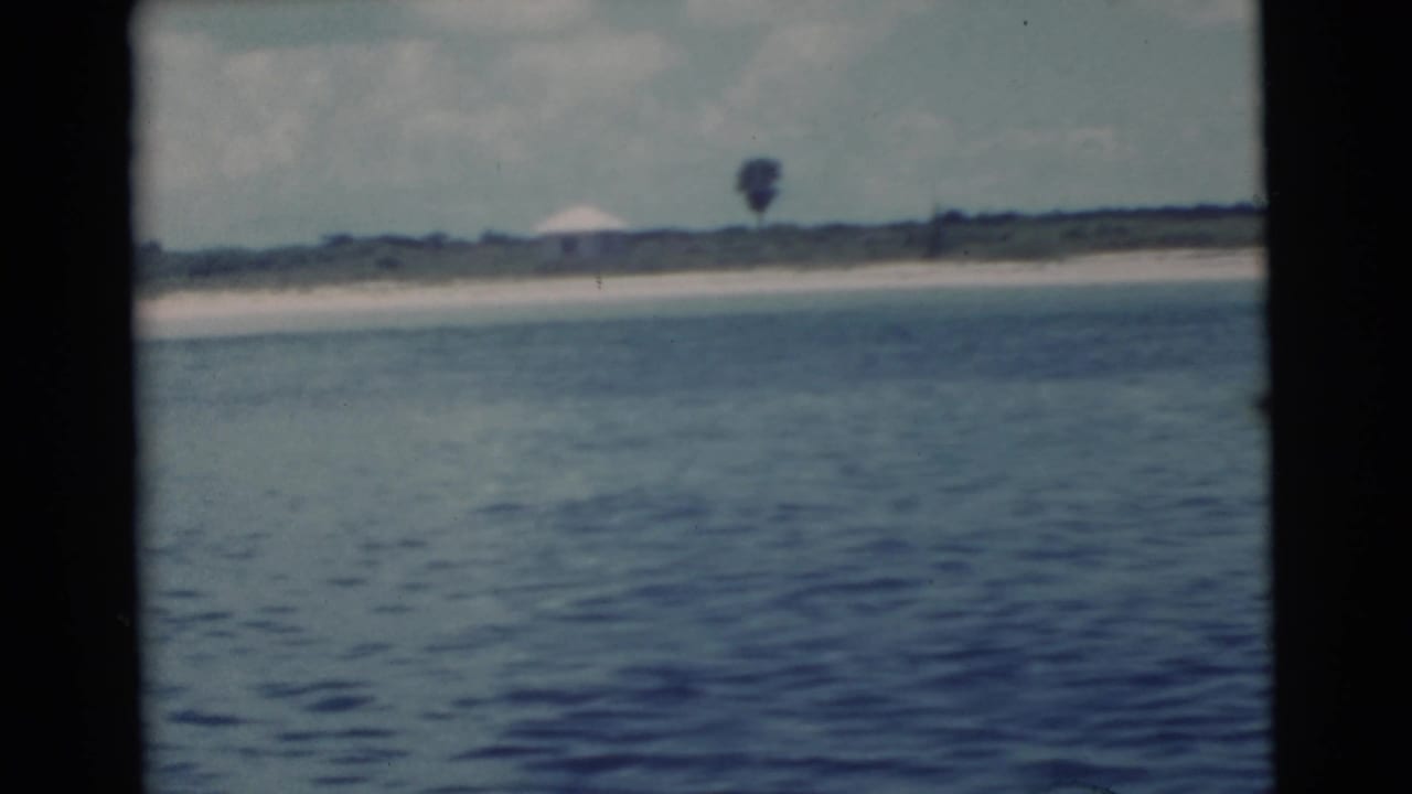 Distant beach with calm water, low shoreline, and a small white structure.