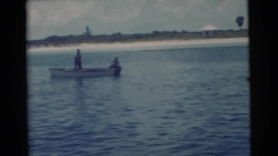 1956 Miami coastal frame showing a small boat with two distant people near the beach.