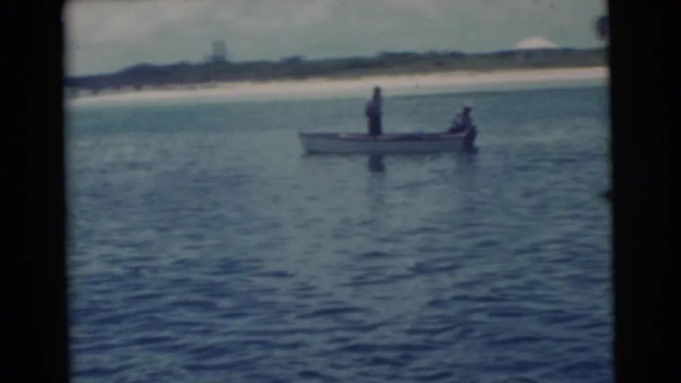 1956 Miami 8mm frame of a small motorboat carrying two distant people near the shore.