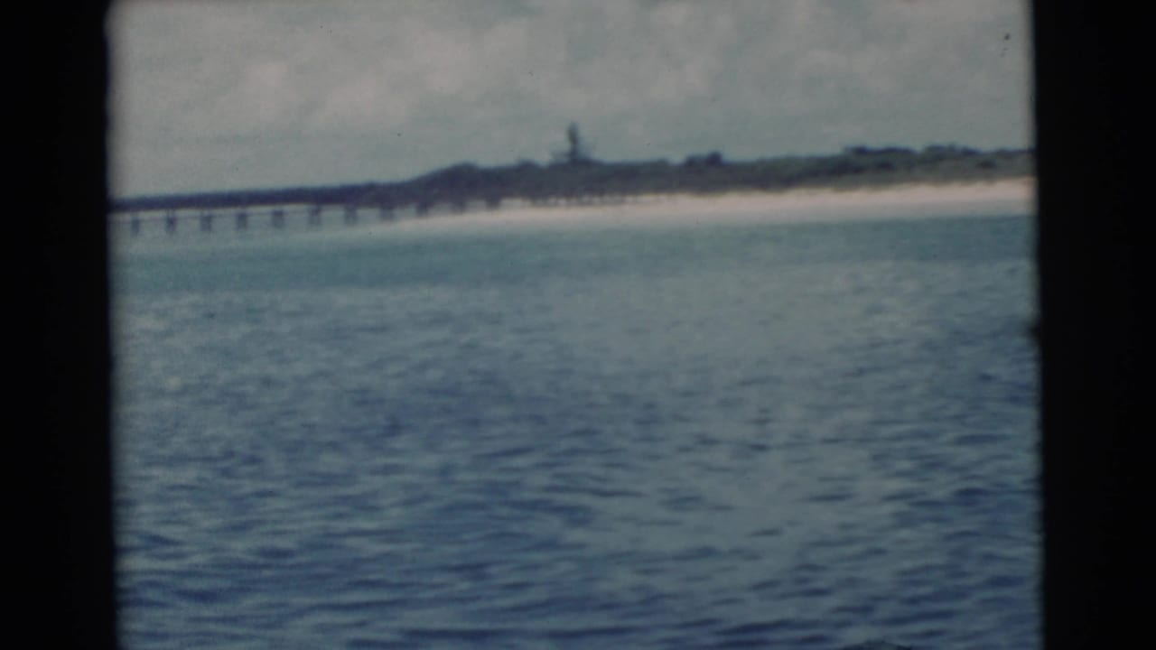 Open water with a long pier and sandy shoreline in the background.