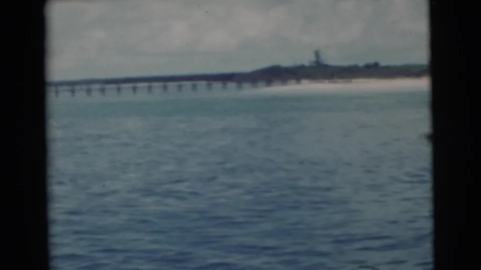 Soft 8mm frame of Miami waterfront, showing rippled water, a long pier, beach, and low coastal structures in the distance.