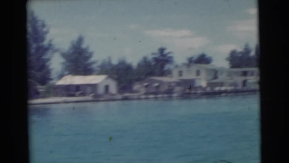 1956 Miami-area shoreline with waterfront houses, docks, trees, and blue-green water seen from a boat.