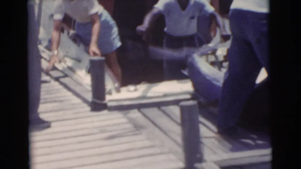 People on a Miami dock handle gear or a catch beside a boat, with dock posts and bright water nearby.