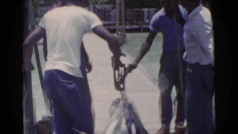 Miami 1956 dockside frame with men coordinating around a large fish as it is positioned near their feet.