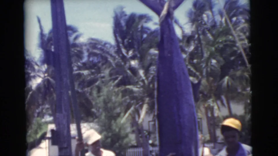 A close, soft 8mm view shows the large marlin and its bill near a tropical Miami dock, with men partly visible below.