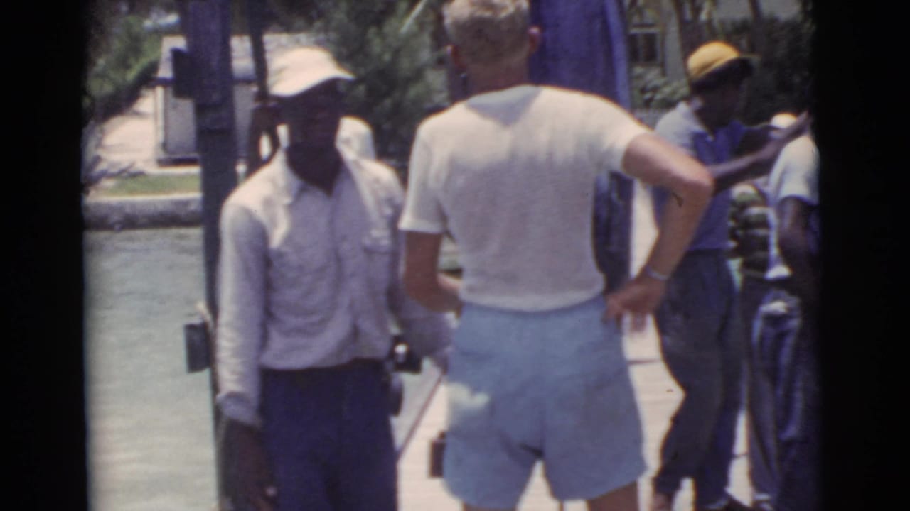 Men standing on a wooden pier beside water, with one man facing away in shorts.