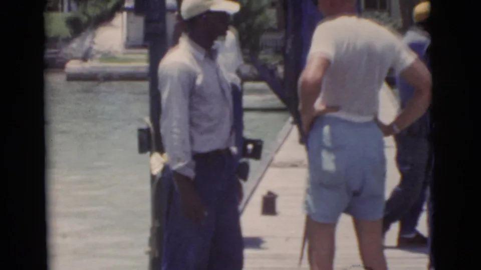 1956 Miami waterfront frame showing men beside an upright billfish or similar large catch on a pier.