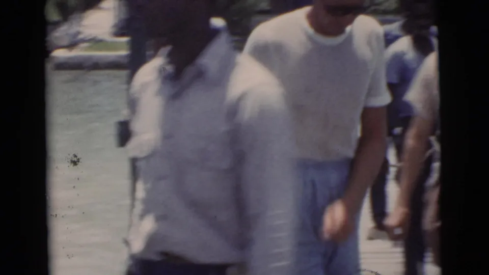 Soft 8mm frame from the Miami pier scene, with men moving close to the handheld camera beside the water.