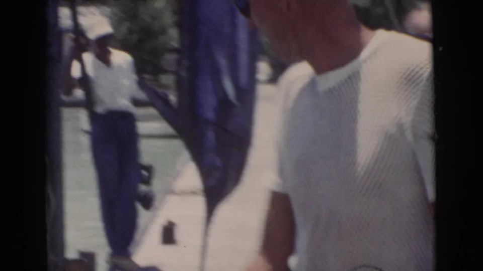 1956 Miami pier frame with a man in a white knit shirt in the foreground and another man near the upright catch.