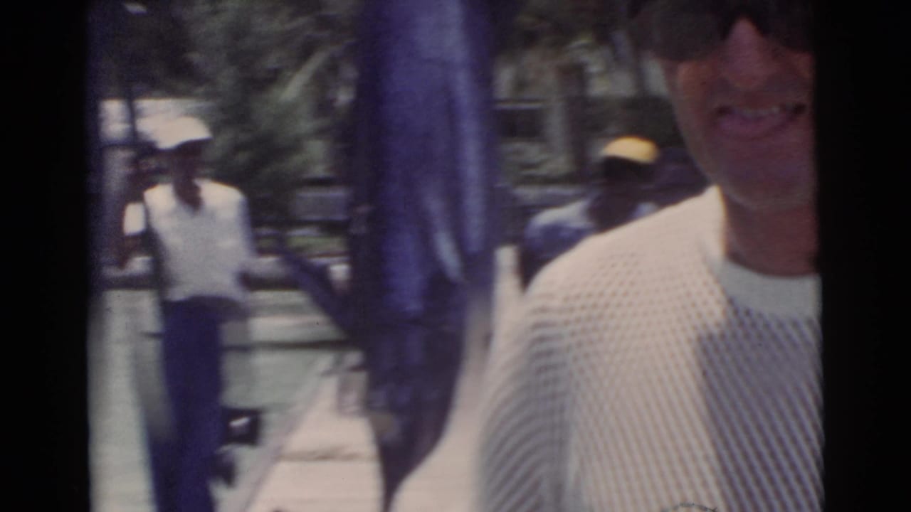 Man partly close to camera near a large hanging marlin on a sunny dock.