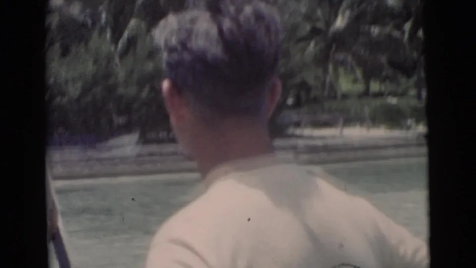 The camera moves close behind a man on the Miami waterfront, with palms and calm water visible ahead.