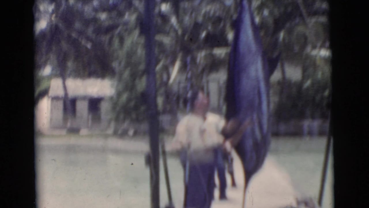 A man in a light shirt stands near a large fish hanging beside a dock.