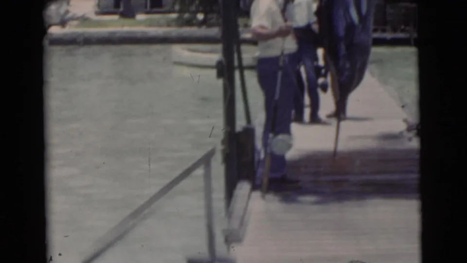Two men remain on the wooden dock beside the large marlin, framed by calm Miami water, dock railings, palms, and soft 8mm blur.