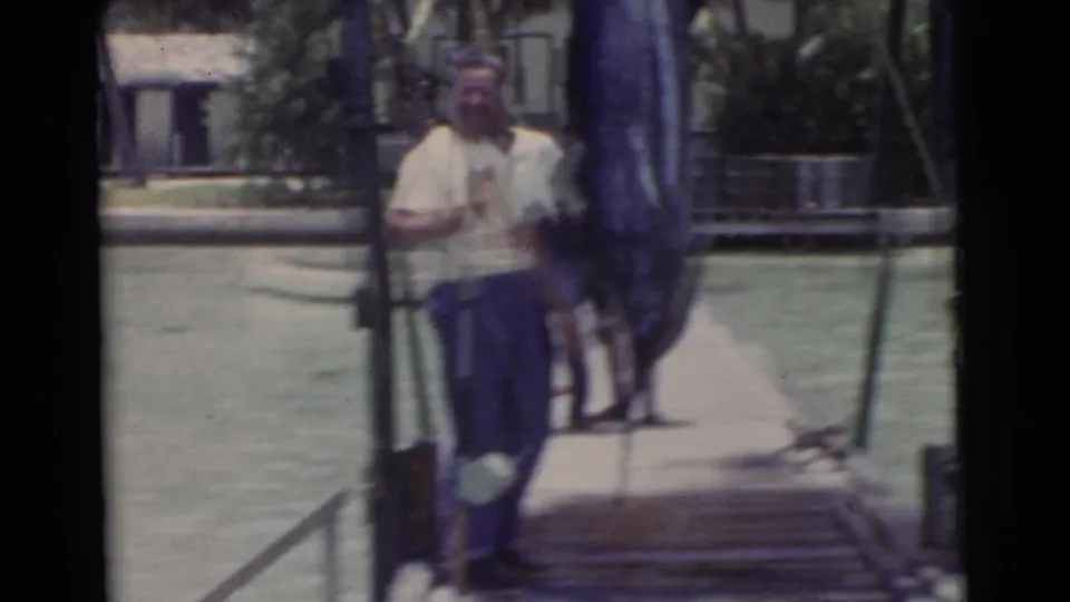 1956 Miami home-movie frame showing men on a wooden pier near water, with soft focus and motion blur.
