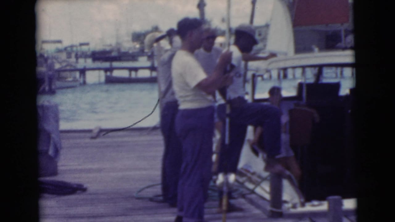 Men on a dock beside a boat cabin, with water and railing behind them.