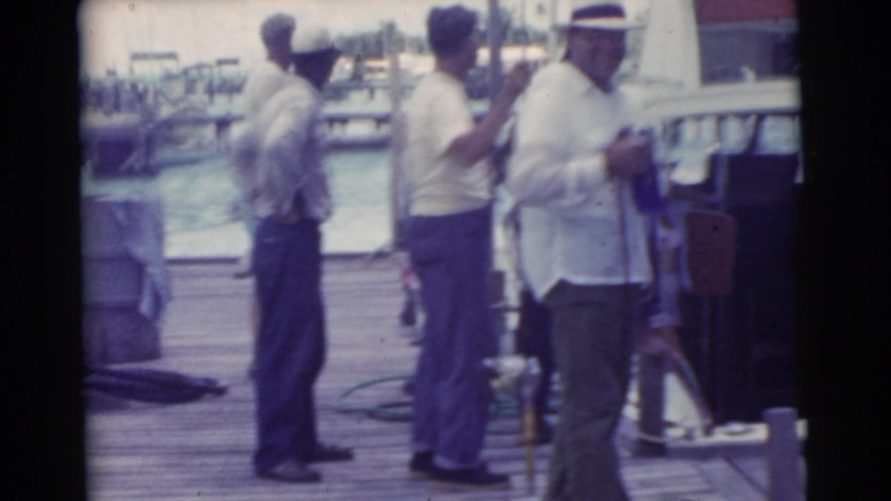 Several men stand on a dock with harbor water and boats behind them.