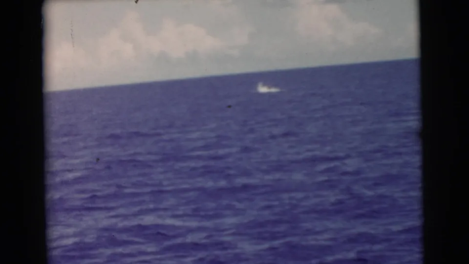 1956 Miami home-movie frame showing dark blue open water, a low horizon, cloudy sky, and a distant white moving object.