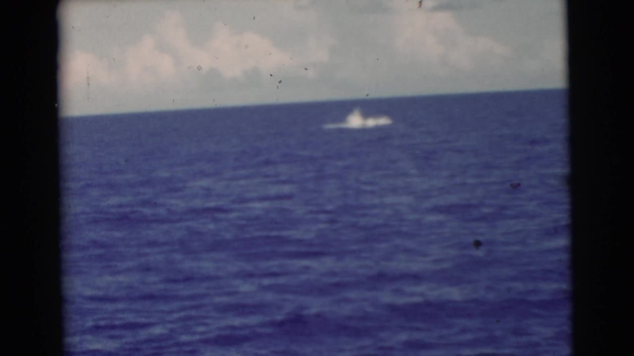 Blue ocean under cloudy sky with a distant white splash near the horizon.