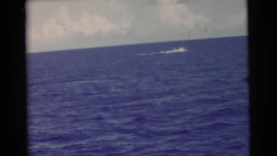 1956 Miami-area home-movie frame shows a distant white splash or wake on open ocean below a pale cloudy sky.
