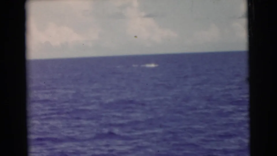 A soft 1956 Miami-area 8mm frame shows blue water, cloudy sky, and a faint white splash far from the camera.