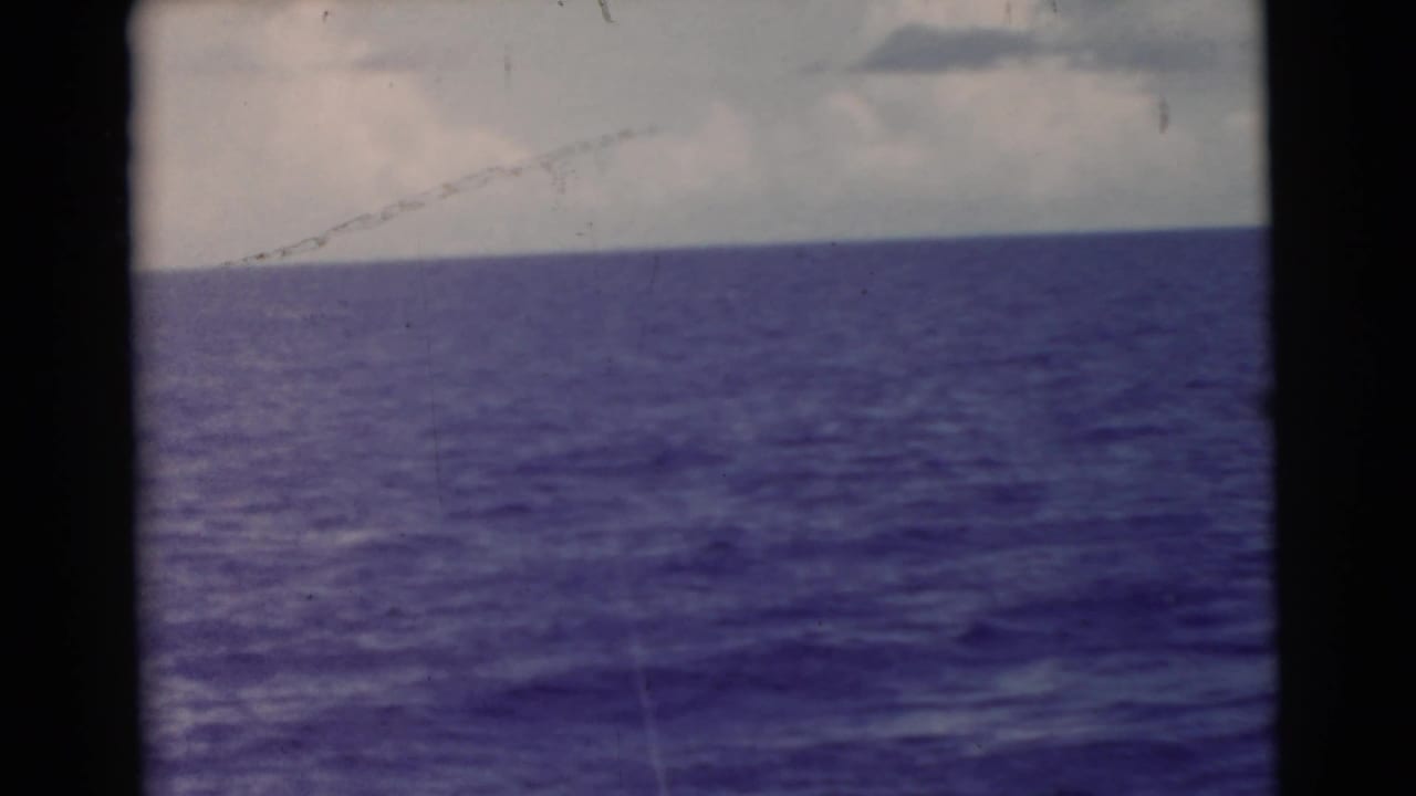 Open ocean under a cloudy sky, framed by dark 8mm film edges.