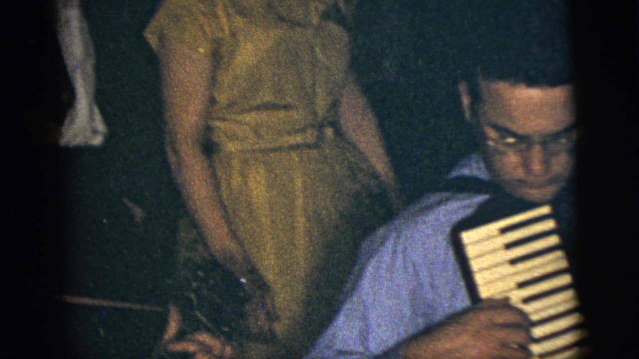 Man in a blue shirt plays accordion while a woman in a yellow dress stands nearby.