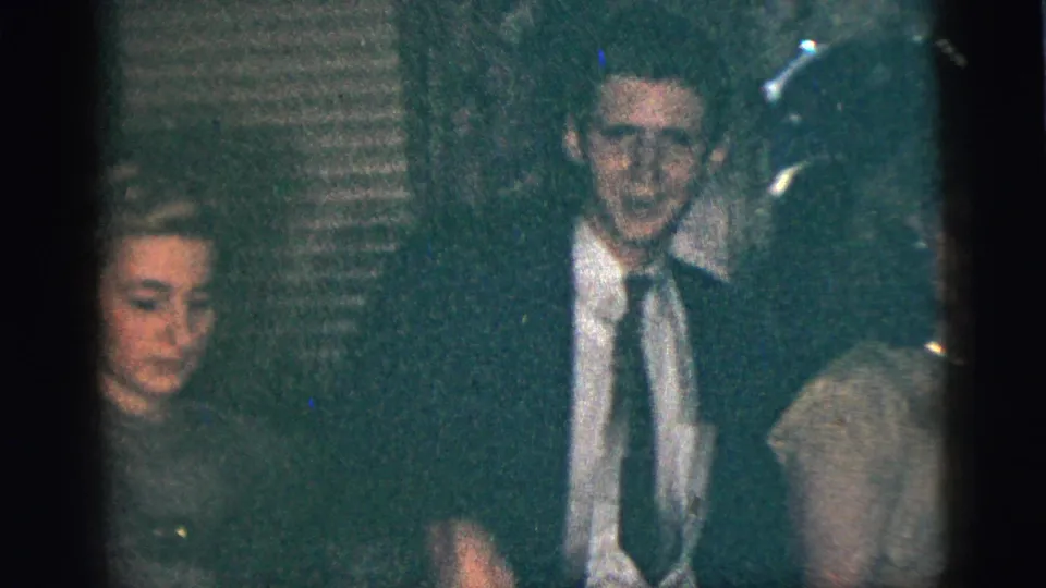 1956 New York City party footage shows guests in suits and dresses gathered in a low-lit private room near a visible microphone.