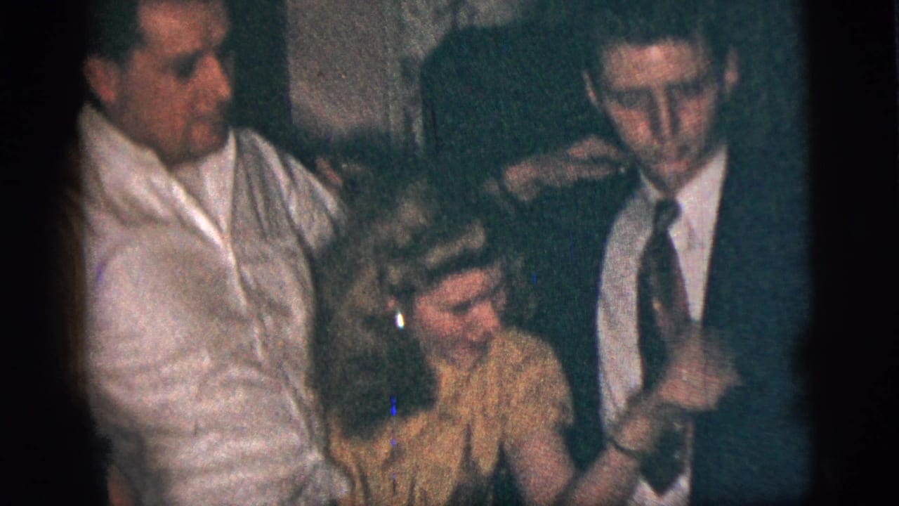 Woman in yellow dress stands between a man in a white shirt and a young man in a suit.