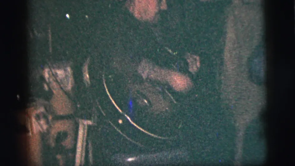 Low-light 8mm frame from a 1956 New York City small venue, with a musician and instrument seen close up.