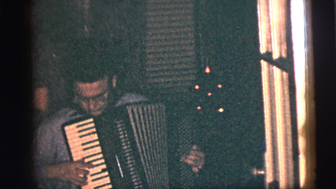 Man seated indoors playing an accordion in a dim room.