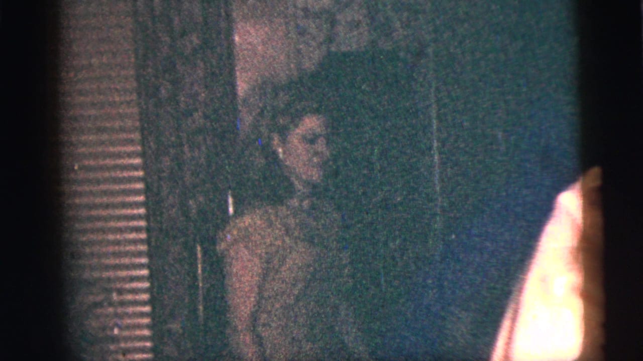 1956 New York City home-movie frame of a woman in profile during a dim indoor party, with another guest partly visible.