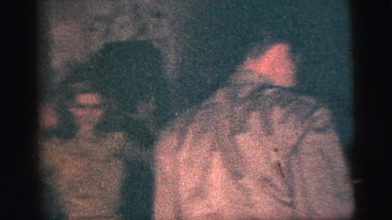 Several people gather indoors, with a man in a light shirt turned partly away from the camera.